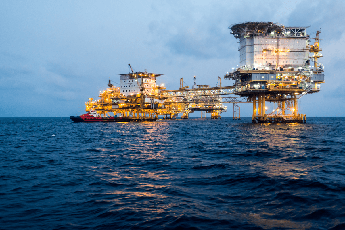 An offshore oil platform illuminated at dusk, showcasing the extensive infrastructure used for extracting oil from beneath the ocean floor.