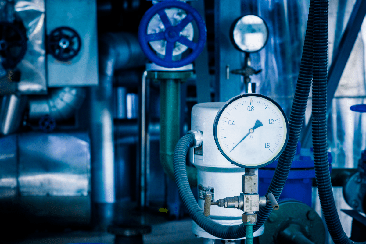 A close-up of an industrial pressure gauge and various pipes and valves in a plant. The image highlights the importance of monitoring and maintaining systems in energy production.