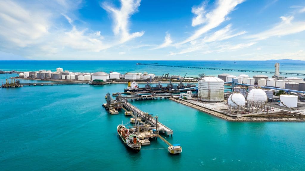 Aerial view of an advanced oil terminal facility with extensive storage tanks, docking platforms, and clear blue waters, illustrating modern oil storage and logistics.